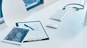 Closeup shot of a clipboard and a digital tablet with brain scans on a desk in a doctor's office
