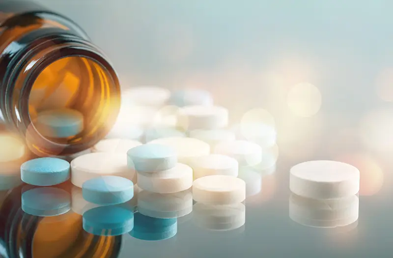 Open pill bottle with pills scattered on a table