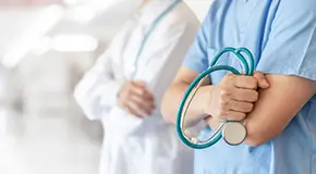 Close-up of medical worker gripping stethoscope while standing next to a doctor