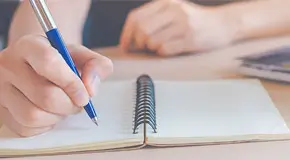Person writing in notebook with a laptop open